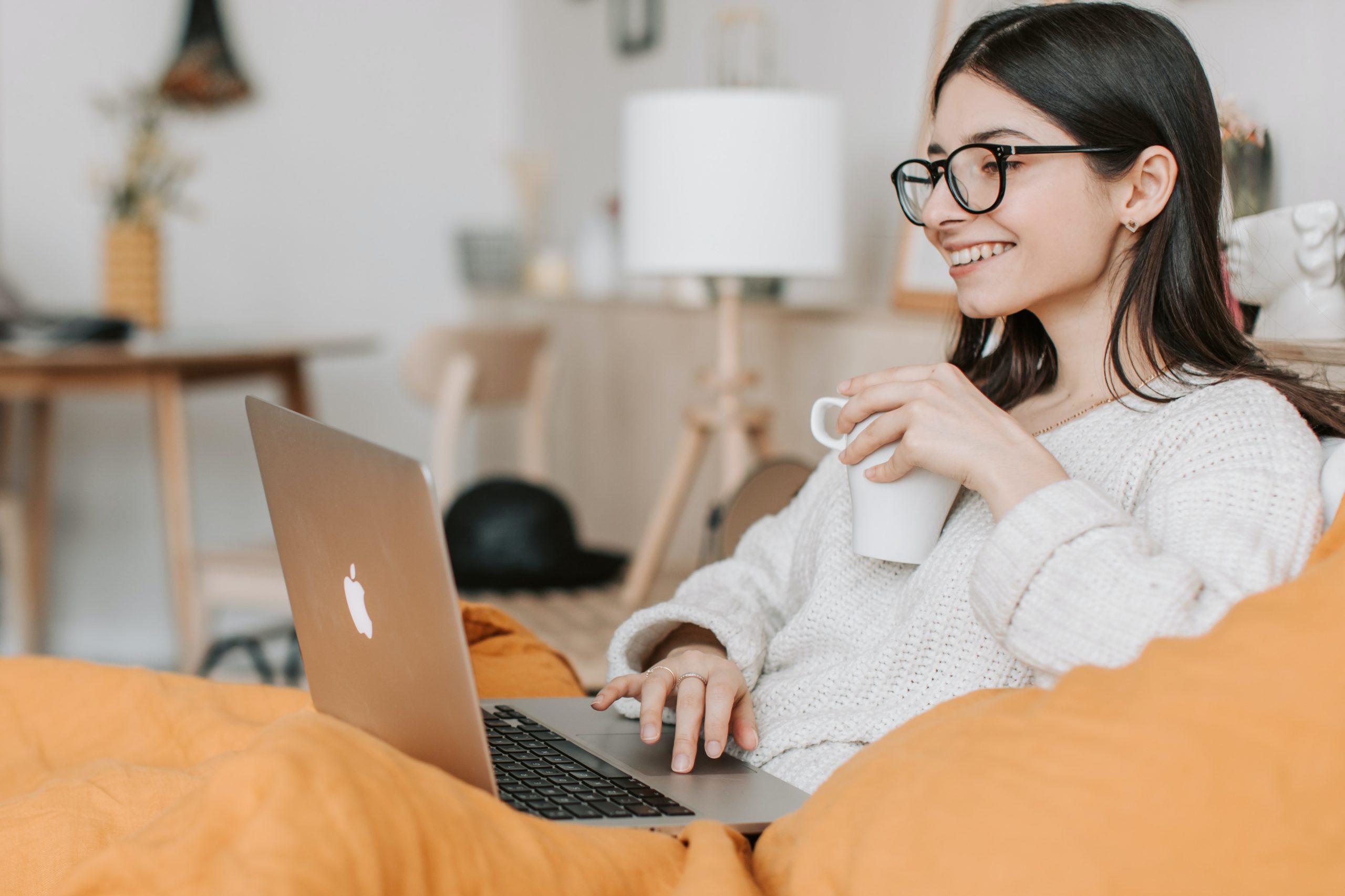 Woman smiling at marketing stats on laptop and drinking tea