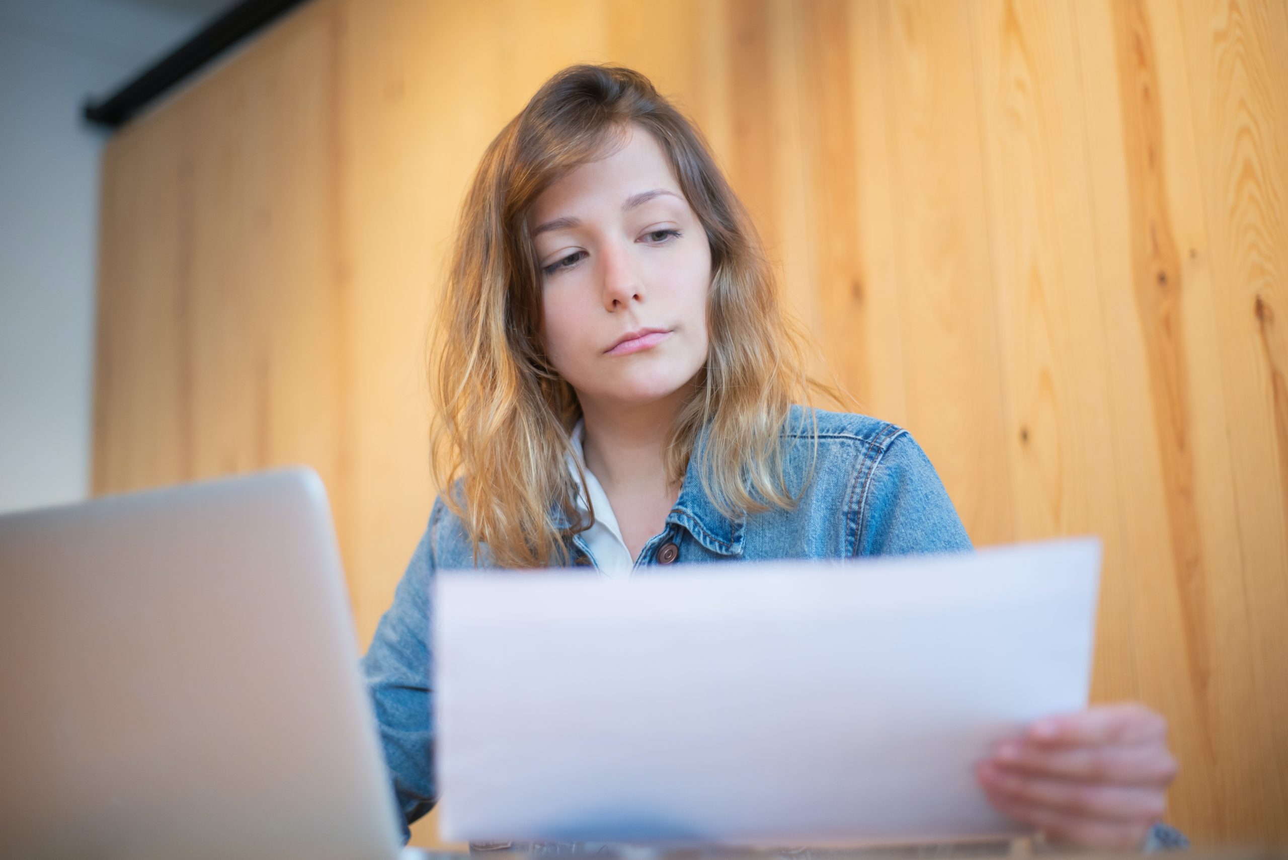 What is social currency - woman in denim jacket looking at a piece of paper whilst sitting at her desk with laptop