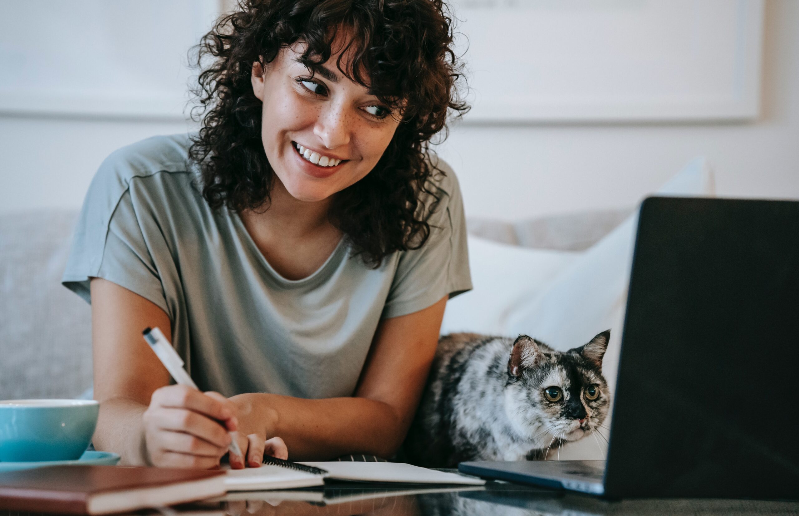 Happy woman watching webinar and making notes with her cat