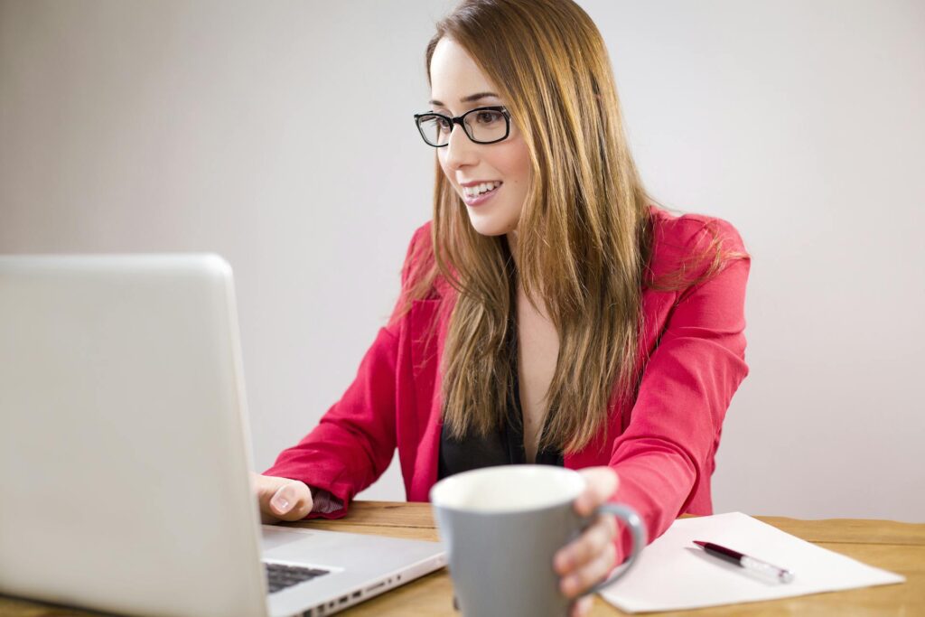 Businesswoman smiling at a desk using a laptop and drinking coffee