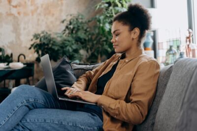 Woman typing a blog on a laptop sitting on a sofa