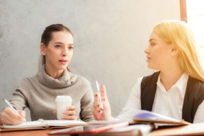 2 women discussing website platform options and writing notes.