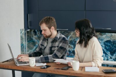A man and woman looking at a laptop with concern, sitting at a bench with coffee.