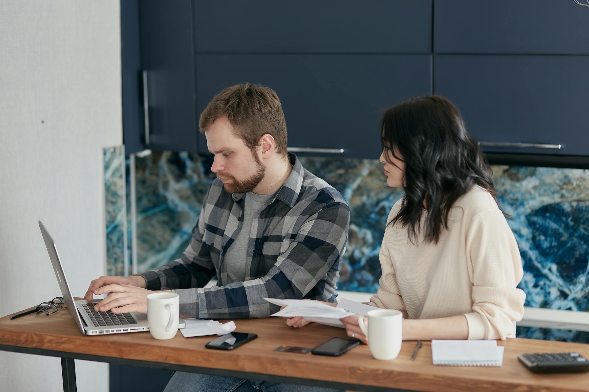 A man and woman looking at a laptop with concern, sitting at a bench with coffee.