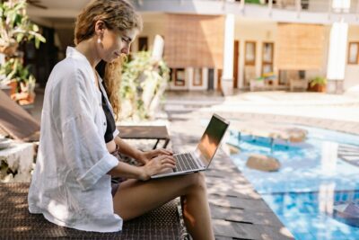 Woman working on a laptop in the shade by the poolside