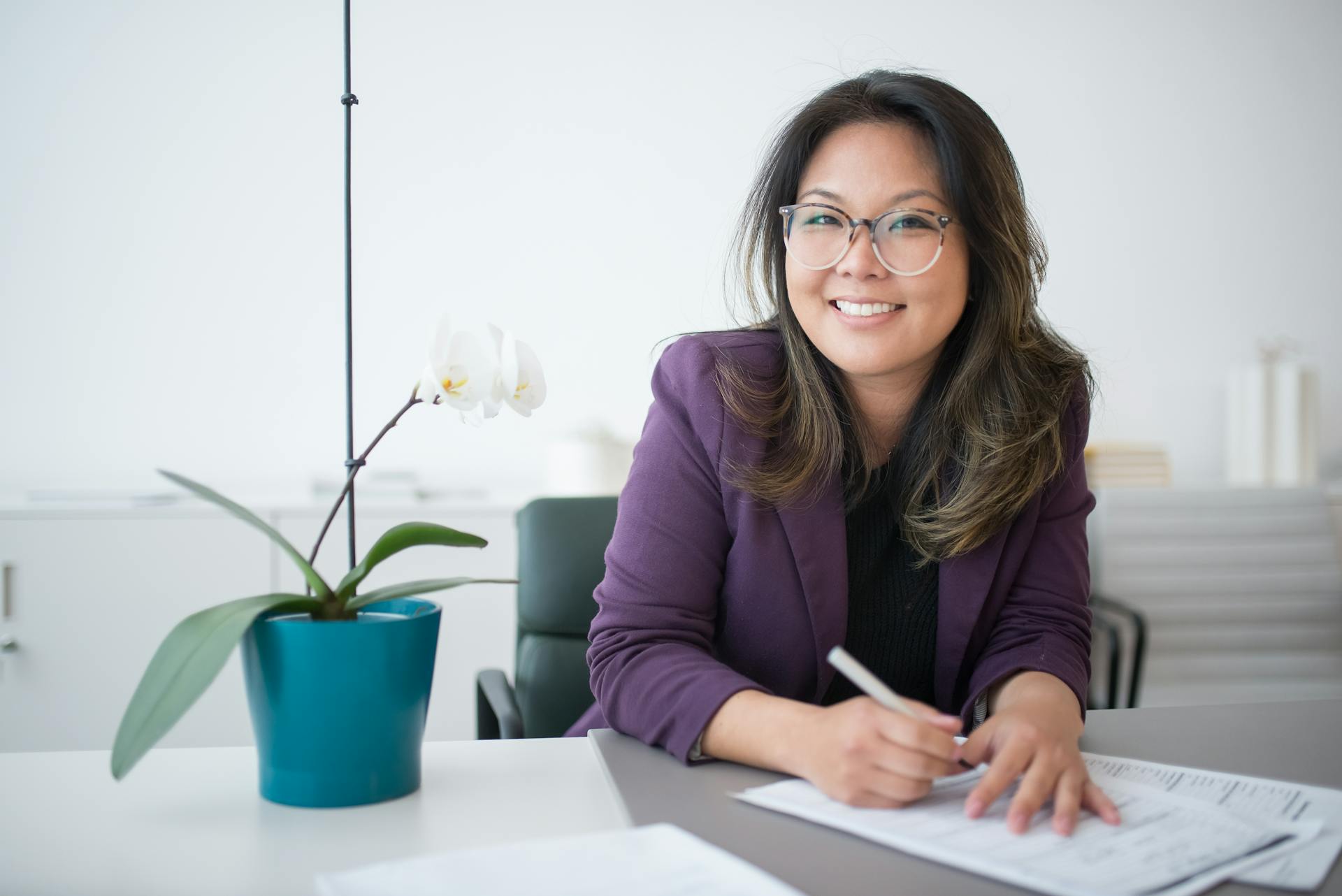 Professional businesswoman sitting at a desk with paperwork and smiling to camera