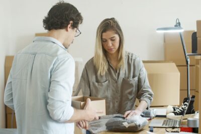 a man and woman preparing e-commerce products for shipping and looking deep in thought.